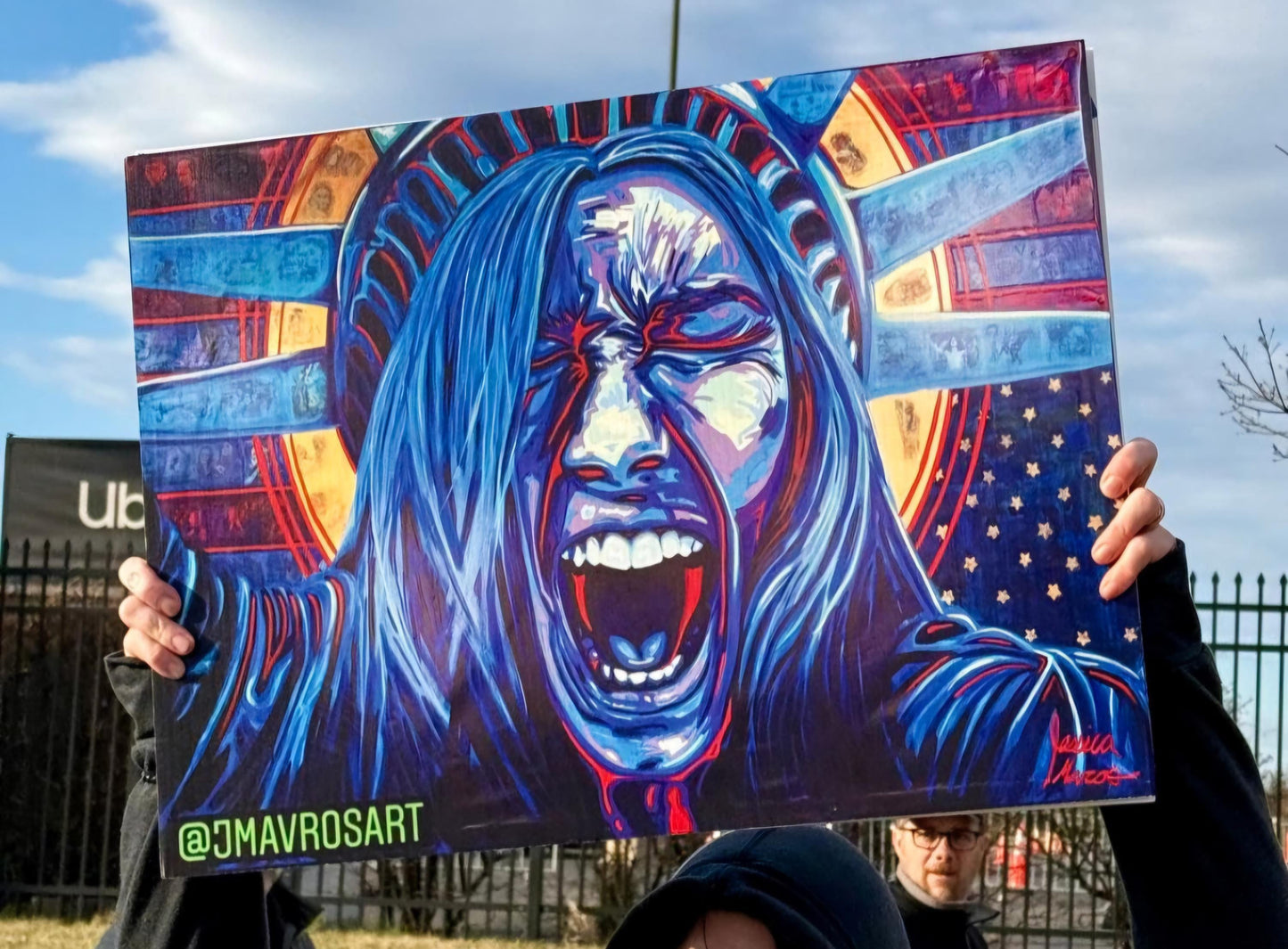 Protester holds vibrantly colored protest art sign by JMAVROSART featuring Lady Liberty screaming against the backdrop of a upside-down usa
Flag